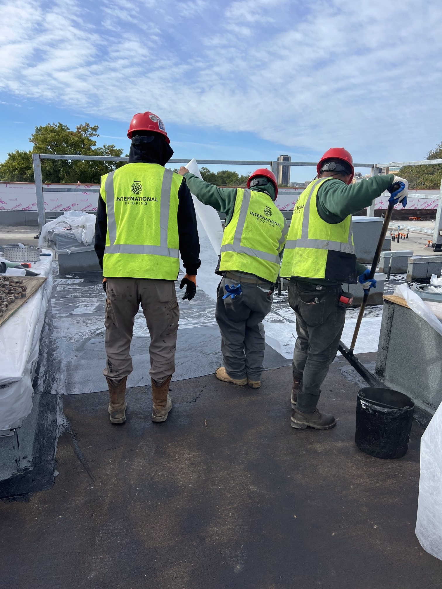 three roofing workers in hard hats and safety vests on jobsite